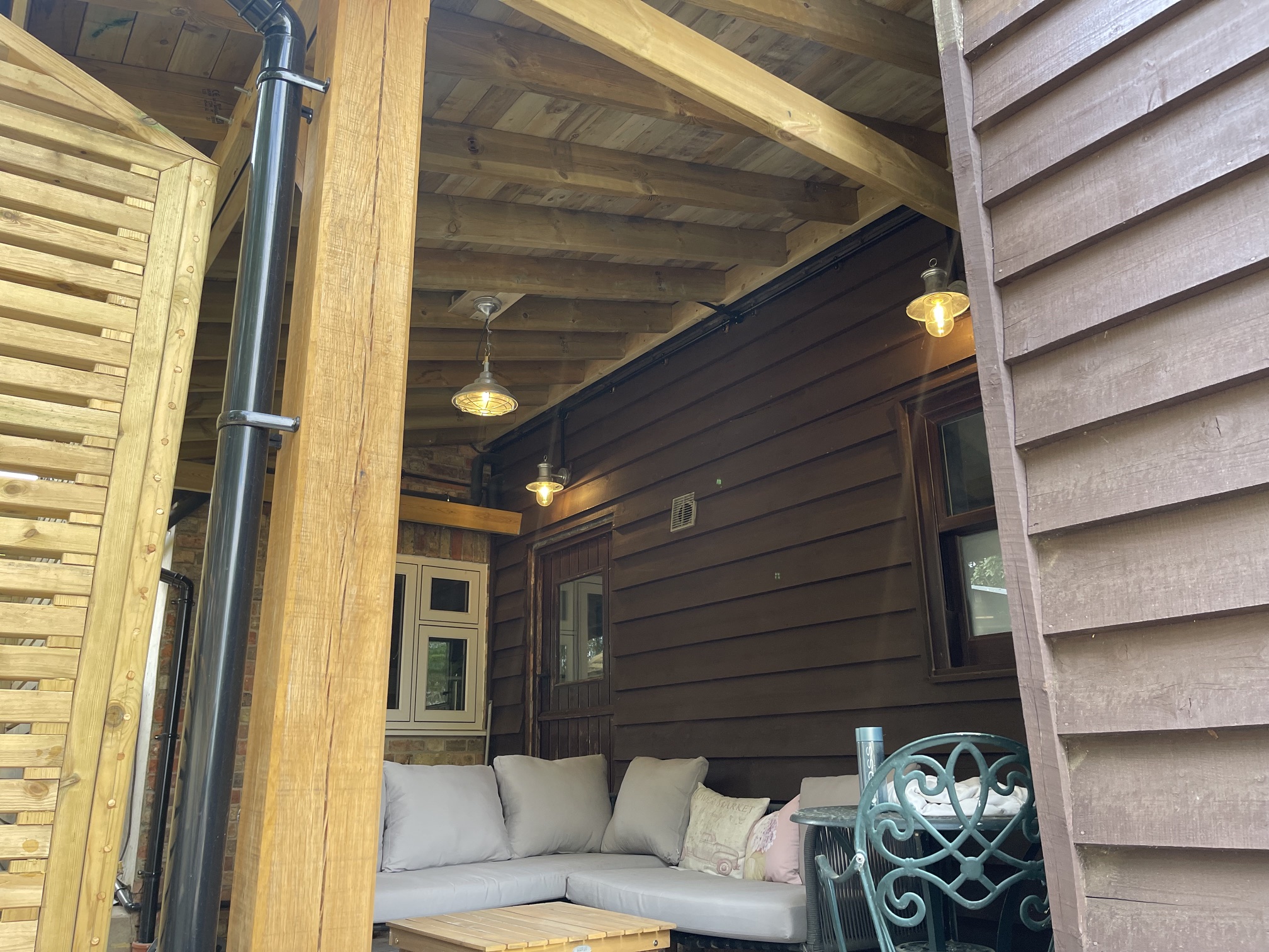 Covered oak-framed car port seating area with exposed timber joists and industrial caged lighting