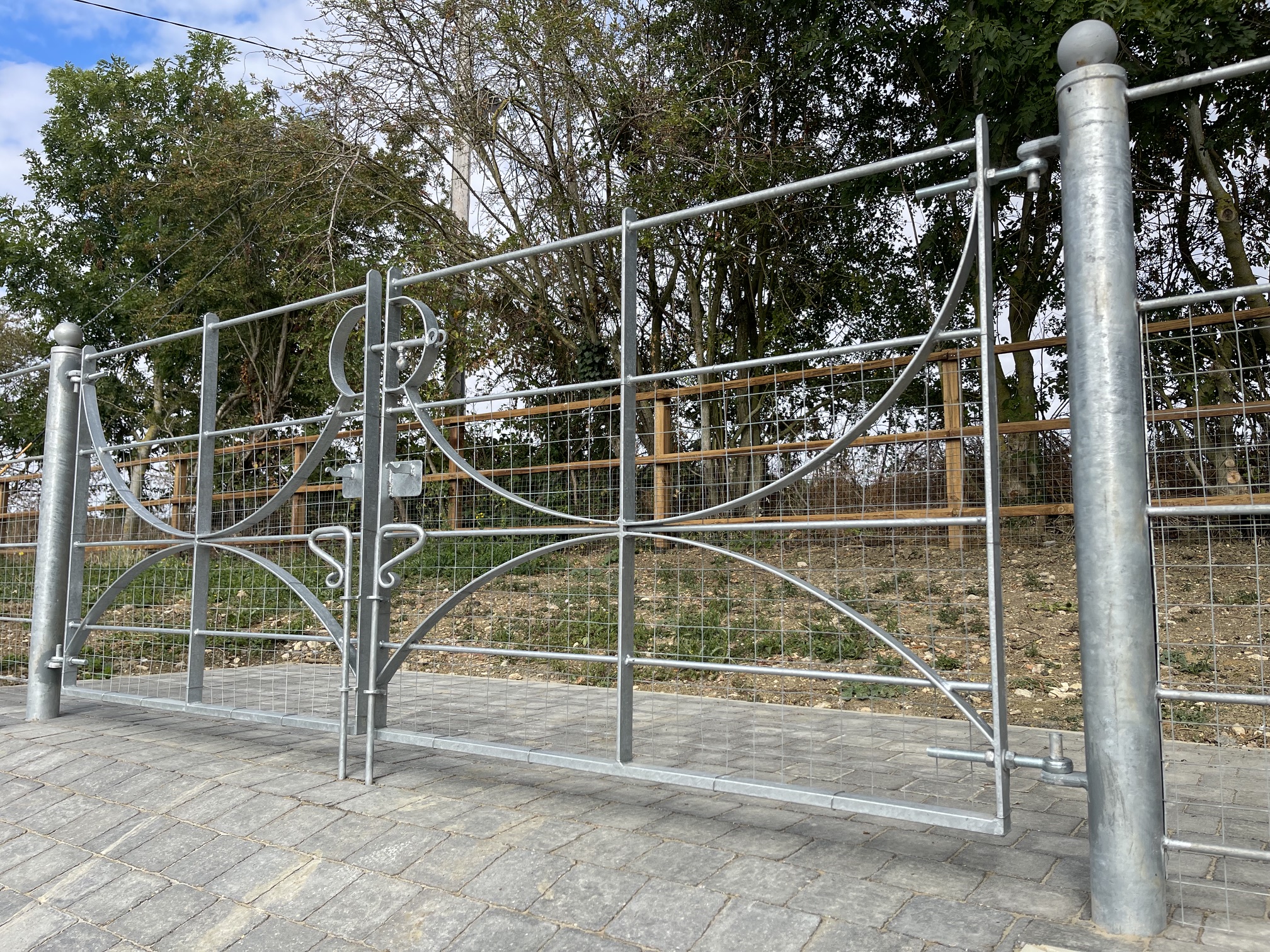 Decorative galvanised metal estate gates with scroll and circle detailing on block paving