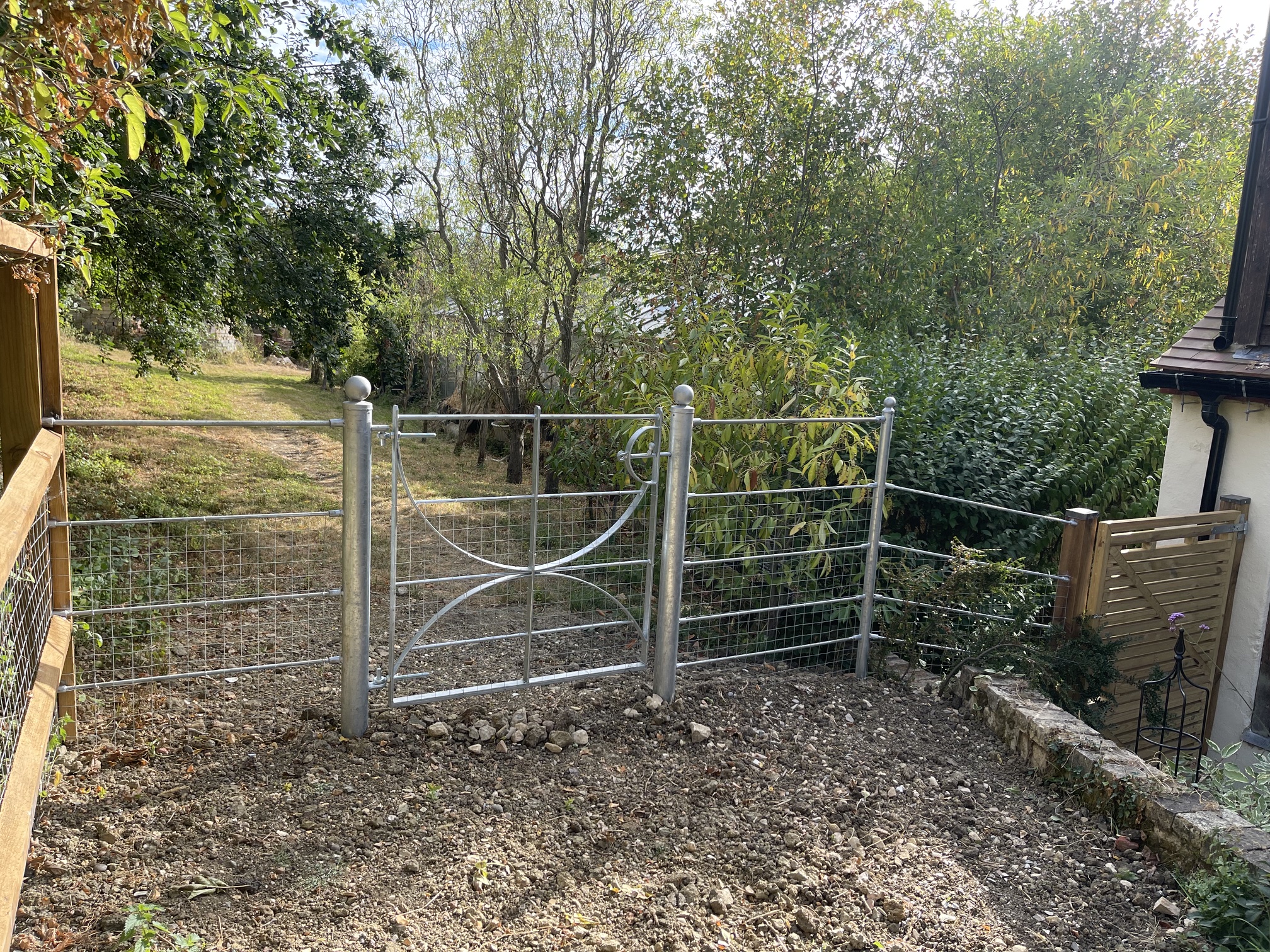 Galvanised metal pedestrian gates with curved bracing and wire-mesh fencing