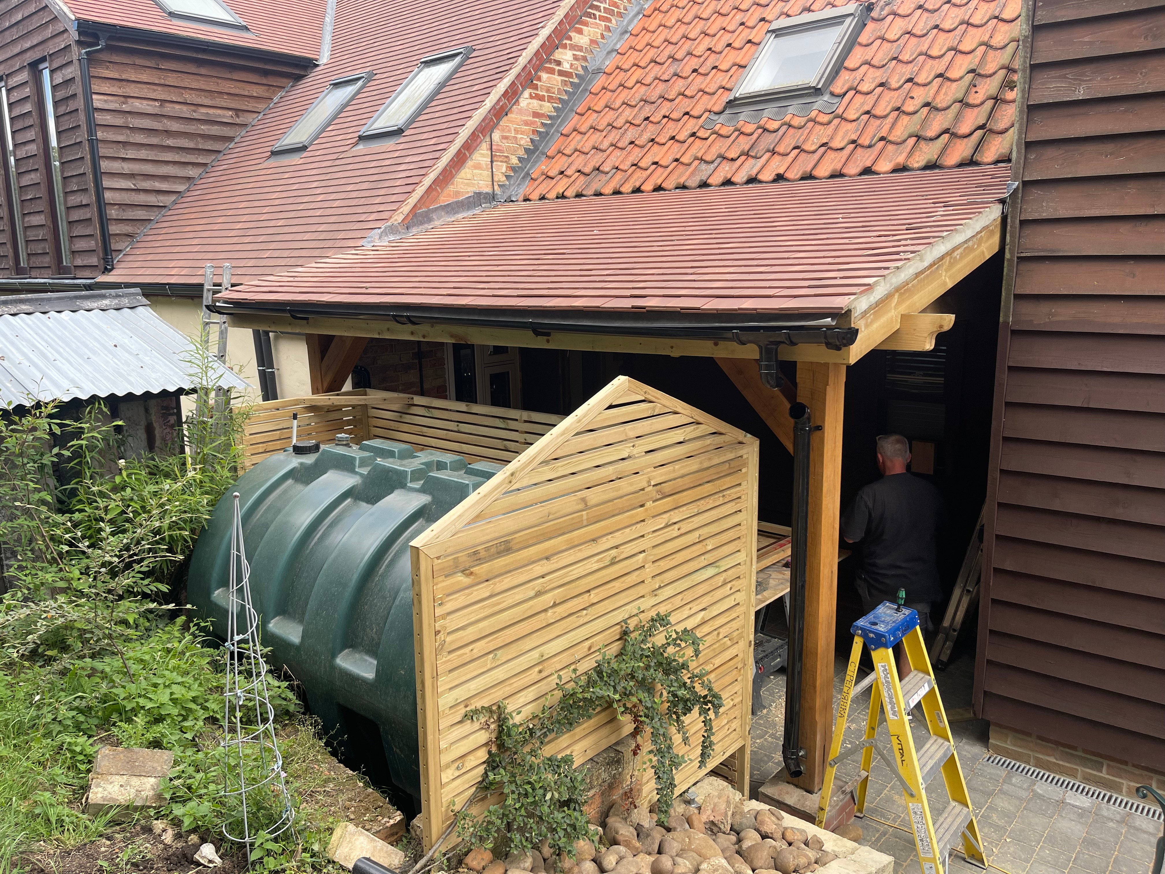 Bespoke timber slatted screen built around an oil tank beside an oak-framed car port