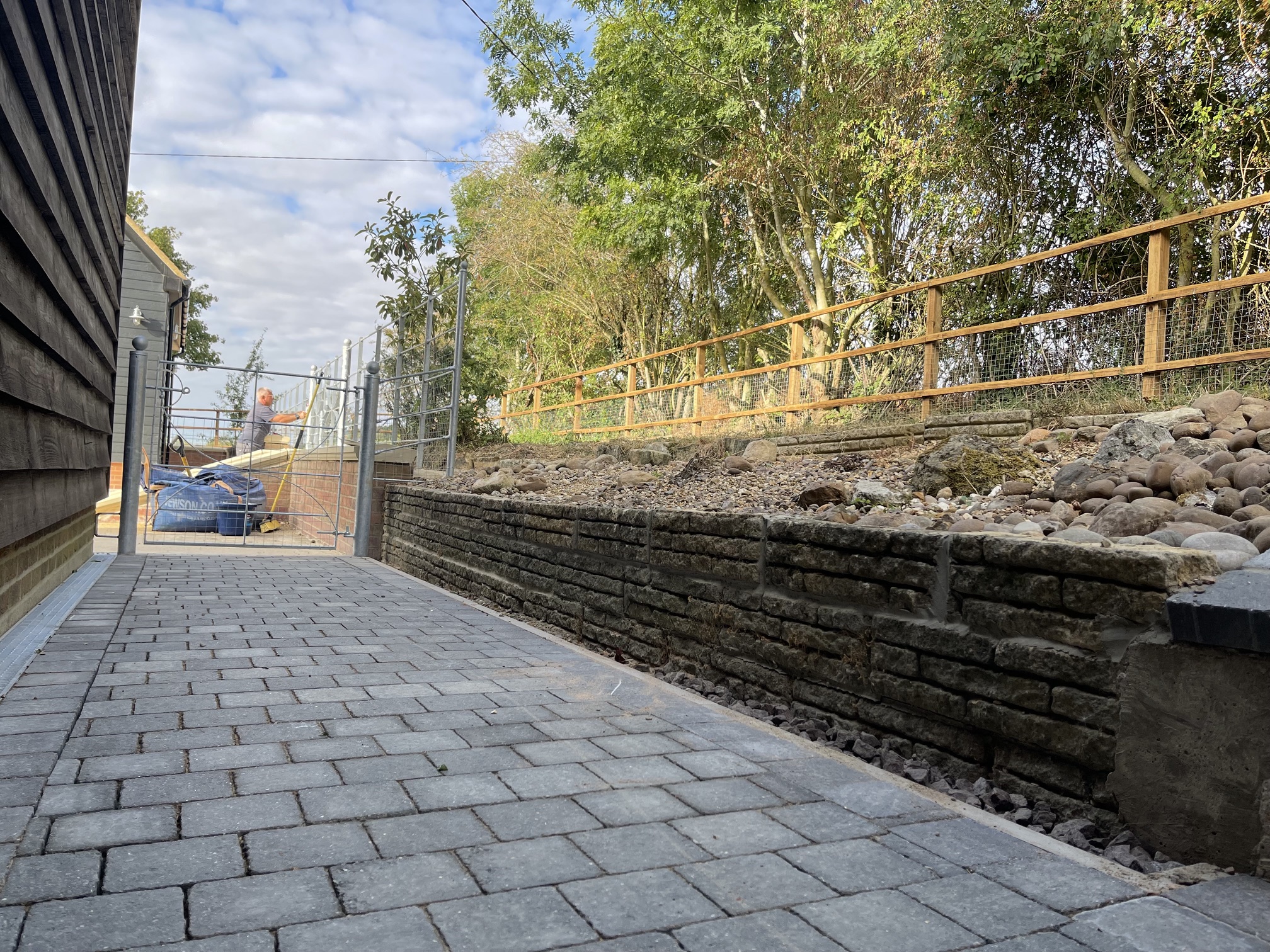 Block-paved pathway alongside a natural stone retaining wall, rockery and timber fence