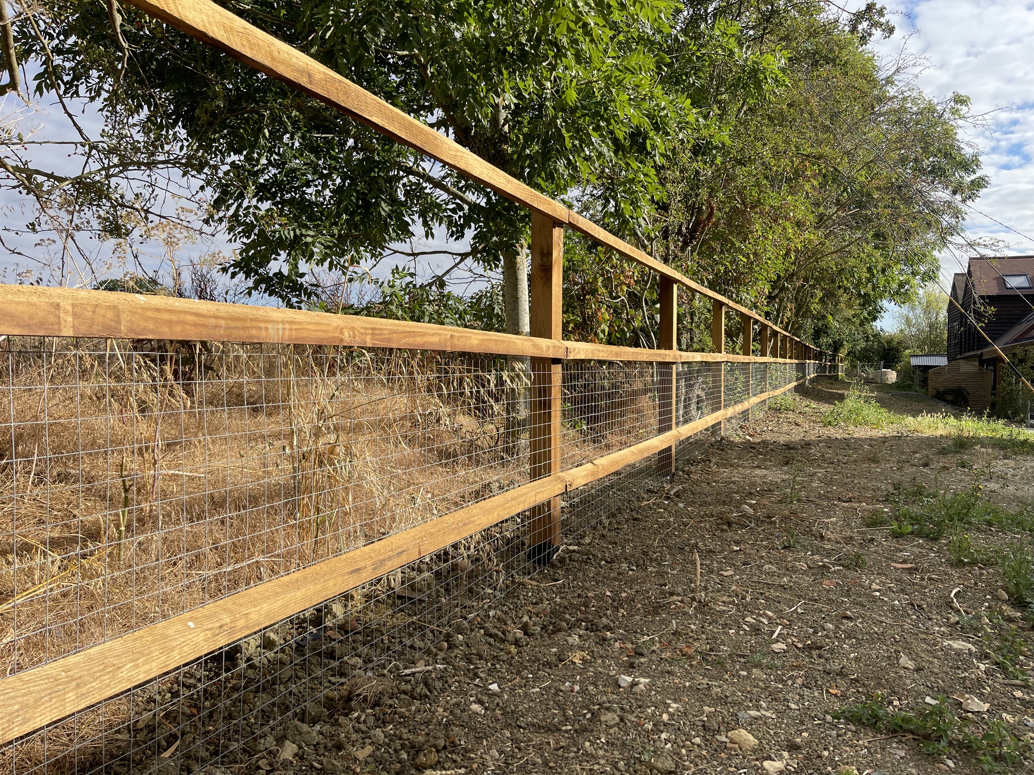 Long timber post-and-rail fence with wire mesh along a wooded boundary