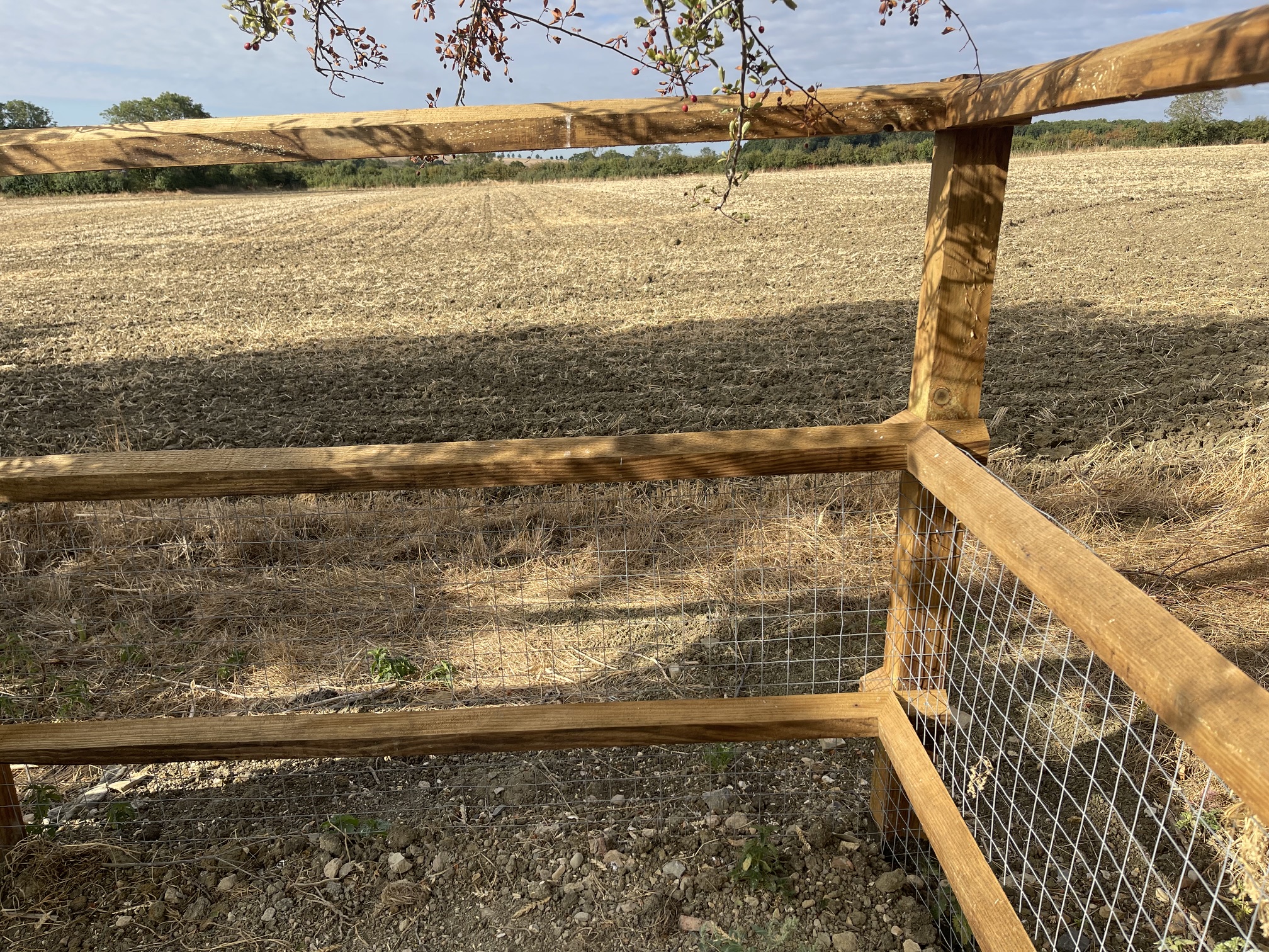 Timber post-and-rail fence with wire mesh overlooking a ploughed field