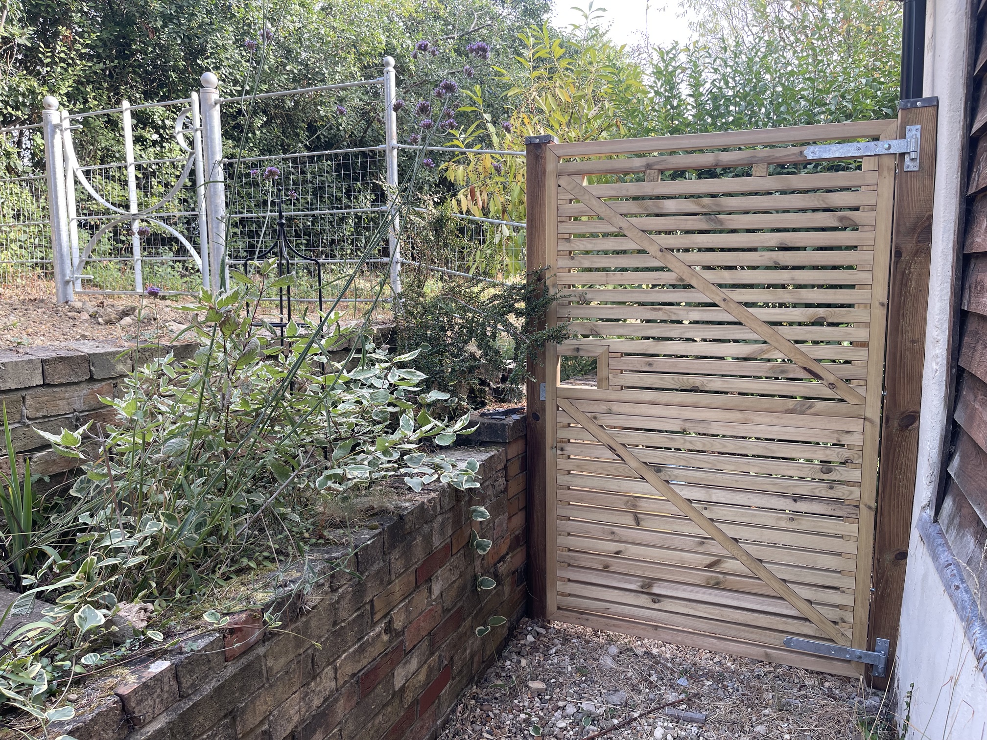 Timber slatted gate on galvanised hinges beside a metal estate gate and brick planter wall